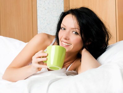 beautiful brunette woman with a cup of coffee in bed